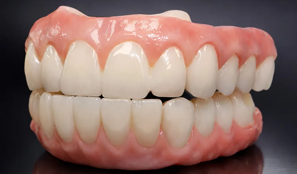 Multi-unit zirconia bridge with hand-finished surface characterization, photographed on a black reflective surface under studio lighting