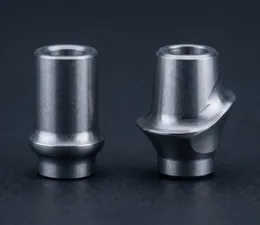 A high-resolution macro photograph comparing two metallic titanium dental implant abutments side-by-side on a dark matte surface. On the left, a stock abutment with a simple cylindrical shape; on the right, a custom-designed abutment featuring an anatomically contoured emergence profile and precise margin shaping.